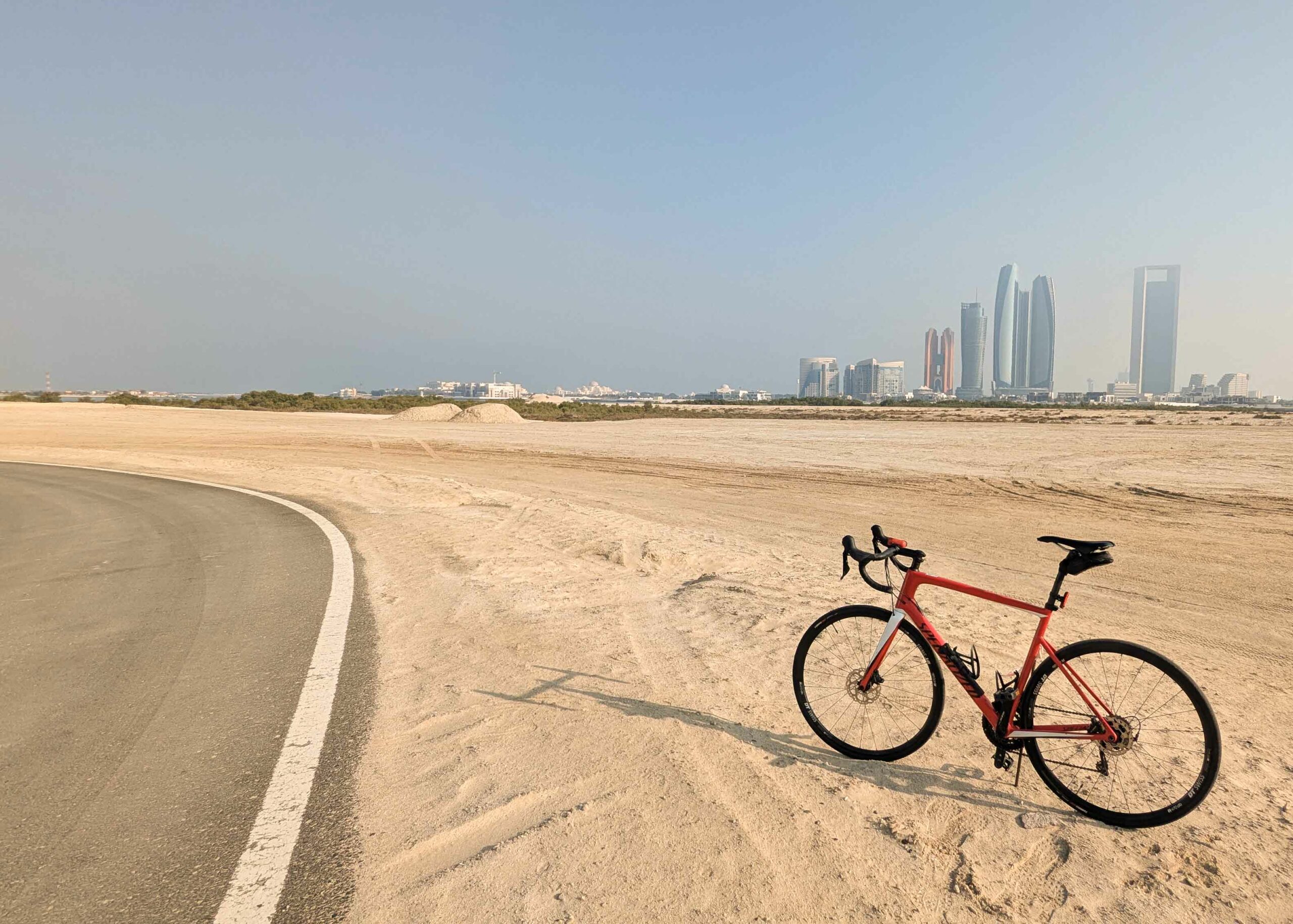 lesvoyagesdapogee-abudhabi-skyline-Al-Hudayriyat-Cycle-Track-michael-paikert-v2 Vélo de route rouge stationné face à la skyline de Dubaï, avec vue sur le Burj Khalifa depuis la promenade de Business Bay