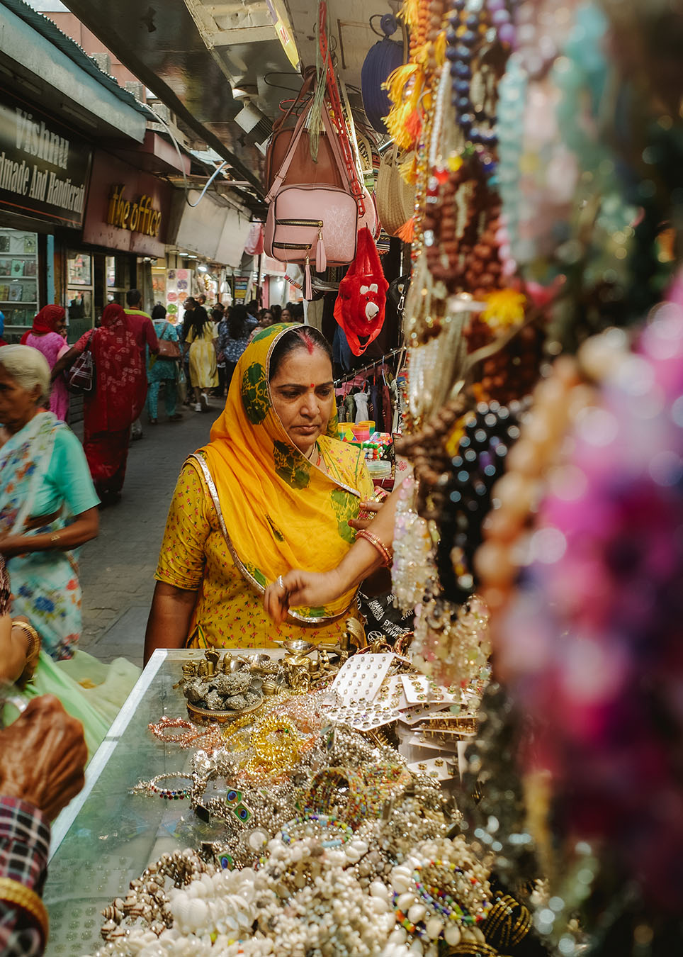 femme-bijoux-bazar-inde-apogeevoyages-r0006366 Femme en sari jaune devant un étal de bijoux dans un bazar de Rishikesh en Inde