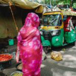 Femme en sari rose dans un marché de Jaipur, en Inde, devant des rickshaws colorés